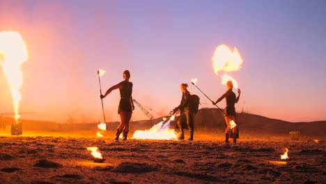 Professional-artists-show-a-fire-show-at-a-summer-festival-on-the-sand-in-slow-motion.-Fourth-person-acrobats-from-circus-work-with-fire-at-night-on-the-beach